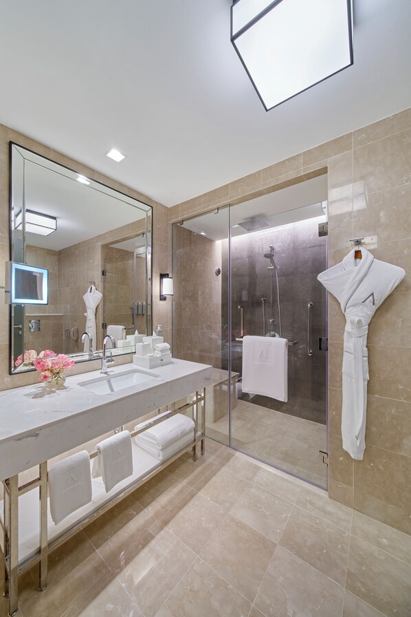 Une salle de bain moderne avec un grand miroir, une douche en verre et un lavabo blanc agrémenté de plusieurs serviettes.