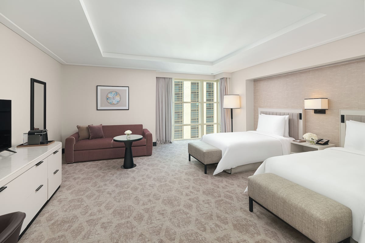 Une chambre d’hôtel avec un lit, un canapé, un bureau, une télévision et une fenêtre avec des rideaux.