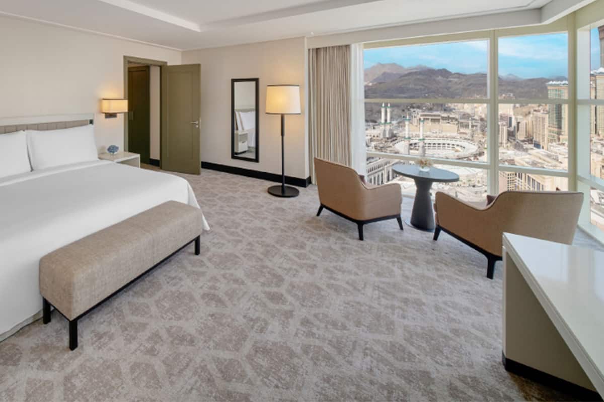 Une chambre d’hôtel avec un grand lit, un bureau, deux chaises, une vue sur la ville et une porte donnant sur une autre pièce.