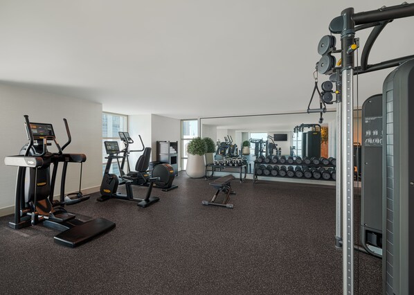 Une salle de sport moderne équipée de machines de cardio, de poids libres et d’un miroir.