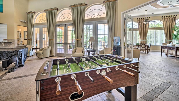 Una habitación amplia con mesa de fútbol, asientos cómodos y ventanas grandes con cortinas.