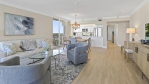 A modern living room with a sofa, armchairs, and a coffee table. There is a dining area with a table and chairs, and a kitchen in the background. - Beautiful 3 bedroom beachfront corner unit-CL0804 (Naples)