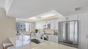 A modern kitchen with white cabinetry, stainless steel appliances, and a large island with bar stools. - Beautiful 3 bedroom beachfront corner unit-CL0804 (Naples)