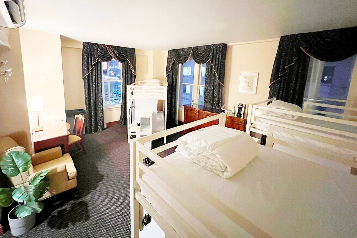 A hotel room with two beds, a desk, a chair, a potted plant, and a view of the outside.