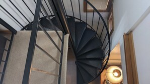 A spiral staircase with a metal railing, carpeted steps, and a pendant light in the background. - Cozy In-Town Condo | Pool | Hot Tub | Sauna (Durango)