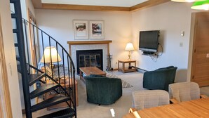 A living room with a fireplace, a TV mounted on the wall, and a staircase. - Cozy In-Town Condo | Pool | Hot Tub | Sauna (Durango)