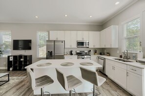 A modern kitchen with white cabinetry, a central island with stools, a built-in oven, and a microwave. - Lavish Atlanta Getaway | 4 BR w/ Fenced Backyard (Atlanta)