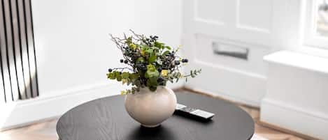 A living room with a round black coffee table, a beige sofa, and a white vase with green foliage and berries.