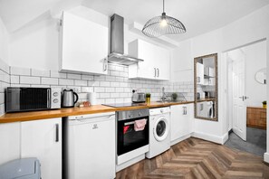 A modern kitchen with white cabinetry, a wooden countertop, a built-in oven, a washing machine, and a large mirror. - Stylish Apartment - Wolverhampton Centre (Birmingham)