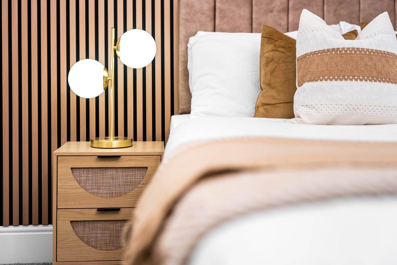 A neatly made bed with a white and brown pillow, a bedside lamp with two round mirrors, and a wooden nightstand with drawers.