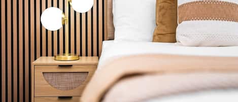 A neatly made bed with a white and brown pillow, a bedside lamp with two round mirrors, and a wooden nightstand with drawers.