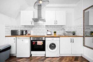A compact kitchen with white cabinetry, a wooden countertop, a built-in washing machine, and a compact dishwasher.