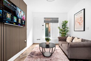 A modern living room with a flat-screen TV, a grey sofa, a round coffee table, and a large window.