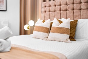 A neatly made bed with white and brown pillows, a wooden headboard, and a wall-mounted light fixture.