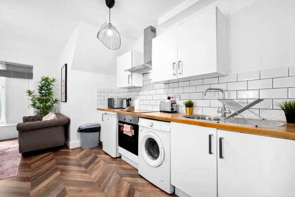 Una cocina moderna con armarios blancos, encimera de madera, lavadora e iluminación colgante.