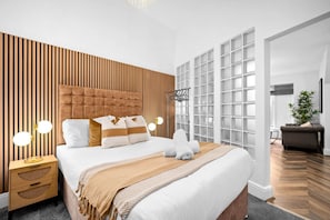 Ein modernes Schlafzimmer mit einem gesteppten Kopfteil, einem großen Bett mit weißen Leinen, einer Wand mit Holzlatten und einem großen Fenster mit Aussicht.