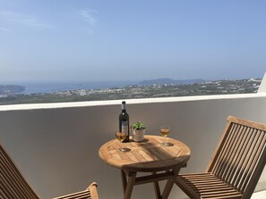 Ein Holztisch mit einer Weinflasche, einem Glas und einem Blumentopf auf einem Balkon mit Blick auf die Küste.
