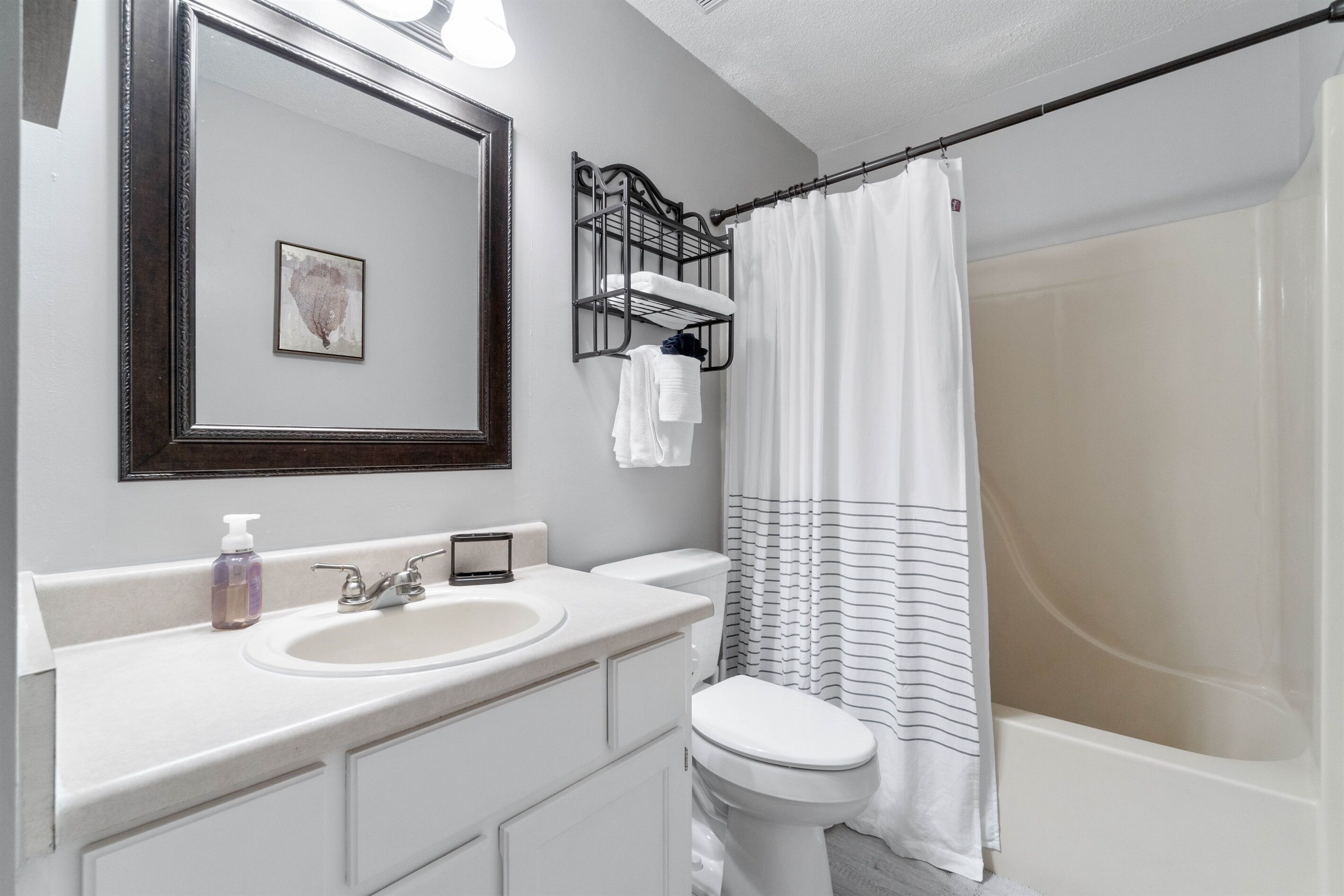 A bathroom with a white sink, a toilet, a mirror, a shower curtain, and a towel rack.