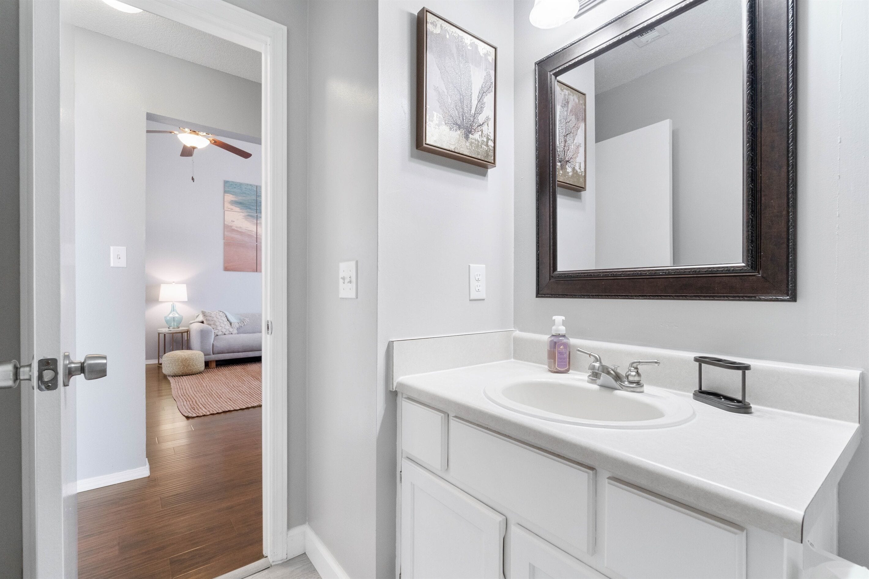 A bathroom with a white sink, a large mirror, and a ceiling fan.