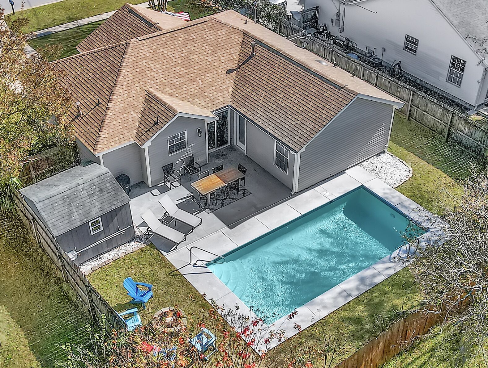A two-story house with a swimming pool, a patio with outdoor furniture, and a fenced yard.