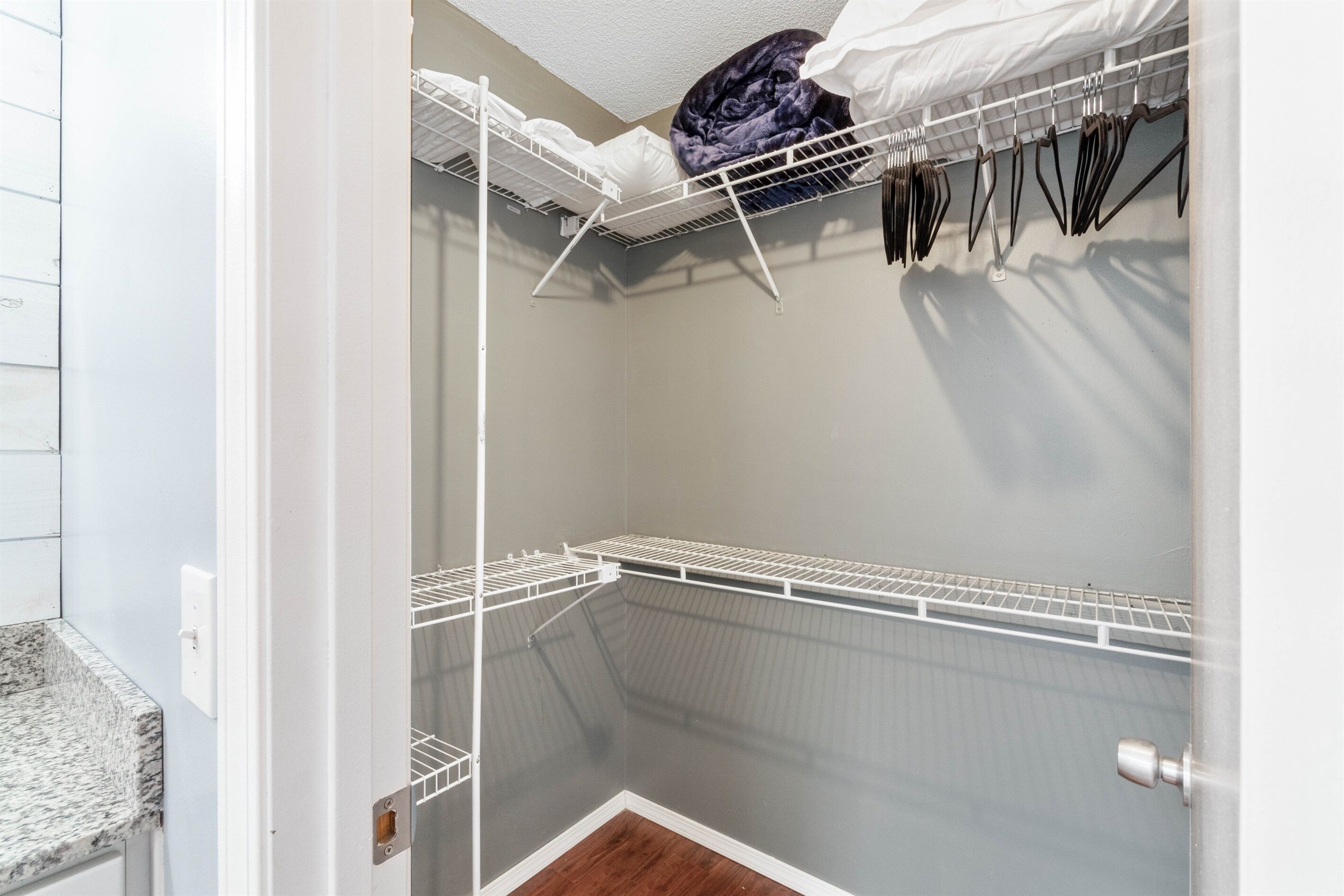 A walk-in closet with white metal shelving units, a hanging rod, and a door with a silver doorknob.