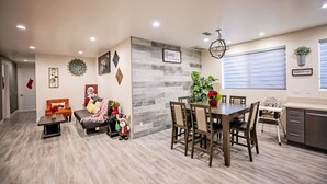 A modern living room with a sofa, a dining table with chairs, and a kitchen area with cabinets and a window. - #2*Disneyland 8minutes*Anaheim Convention*Knott*Beaches (Anaheim)