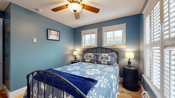 A bedroom with a bed, two windows, a ceiling fan, and a nightstand with a lamp. - Smooth Sailing on the Lake! Free EV charging! (Plattsburgh)