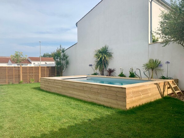 A rectangular swimming pool with a wooden deck, surrounded by a well-maintained lawn and various potted plants.