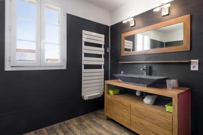 A modern bathroom with a black and white color scheme, a large mirror, a wooden vanity, and a window with a view of the outside.