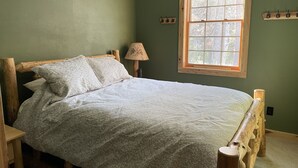 Ein Bett mit Holzrahmen, ein Fenster mit Holzrahmen und eine Lampe auf einem Nachttisch.