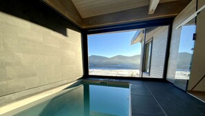 Piscina interior moderna com vista desobstruída para uma paisagem nevada e montanhas através de amplas janelas.
