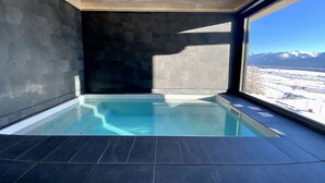 Piscina interior moderna com vista para montanhas cobertas de neve.