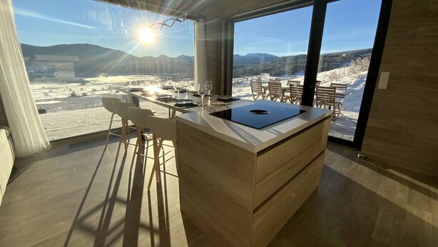 Cozinha moderna com uma ilha grande, banquetas e vista para uma paisagem coberta de neve.