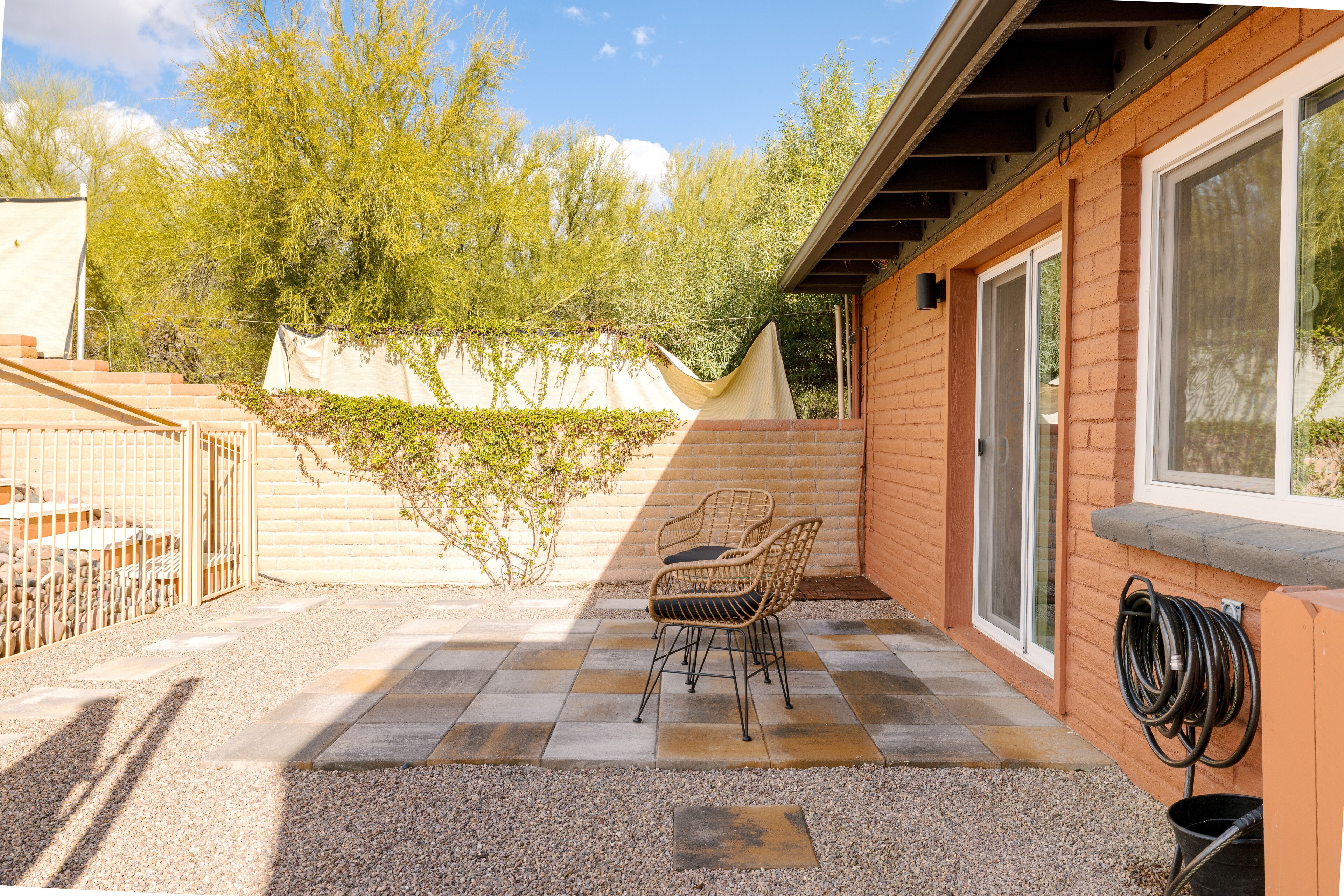 Un patio con due sedie in vimini, un avvolgi tubo e un vialetto sterrato che conduce a un'area recintata.