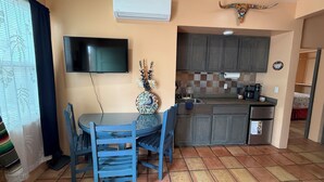 A compact kitchen with a dining area, a flat-screen TV, and a decorative wall piece.