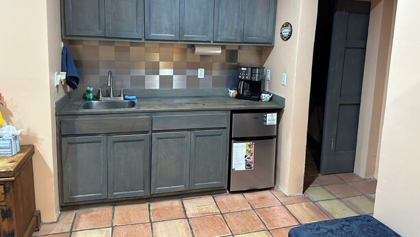 A compact kitchen with dark cabinets, a stainless steel sink, a coffee maker, and a refrigerator.
