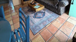 A living room with a patterned sofa, a wooden coffee table, blue chairs, a decorative rug, a ceiling fan, and a wall-mounted painting.