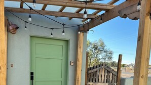 A green door with a small window, a wooden pergola with string lights, and a brick pathway leading to a wooden gate.