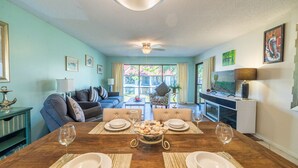 A dining area with a wooden table set for four, a ceiling fan, and a view of the outdoor patio.