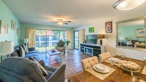 A spacious living room with a dining area, a ceiling fan, and a TV.