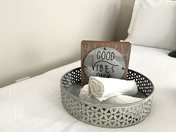A bed with a decorative tray containing a towel and a sign that reads "GOOD VIBES ONLY".