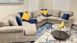 Ein Wohnzimmer mit einem beigefarbenen Ecksofa, einem Glastisch und einem Teppich mit blau-weißen Mustern.