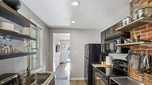 A modern kitchen with stainless steel appliances, a brick accent wall, and built-in shelves. - Co's Corner (Baltimore)