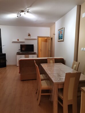 Zona pranzo con tavolo e sedie in legno, televisore su un mobile e porta che conduce in un'altra stanza.