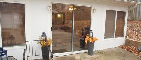 A covered patio area with a sliding glass door, a metal chair, and a planter with autumn leaves.