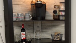 Une cuisine avec un pare-feu en bois, une machine à café, une bouteille de vin et un appareil à café.