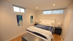 Une chambre à coucher comprenant un lit, deux tables de chevet, un banc et des œuvres d’art accrochées aux murs.