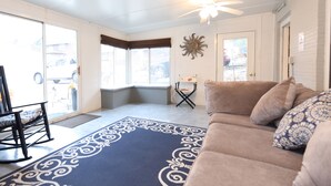 Un salon avec un canapé beige, un tapis à motifs et un ventilateur de plafond.