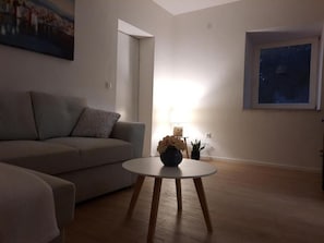 Una sala de estar con un sofá gris, una mesa redonda de madera y un cuadro en la pared.