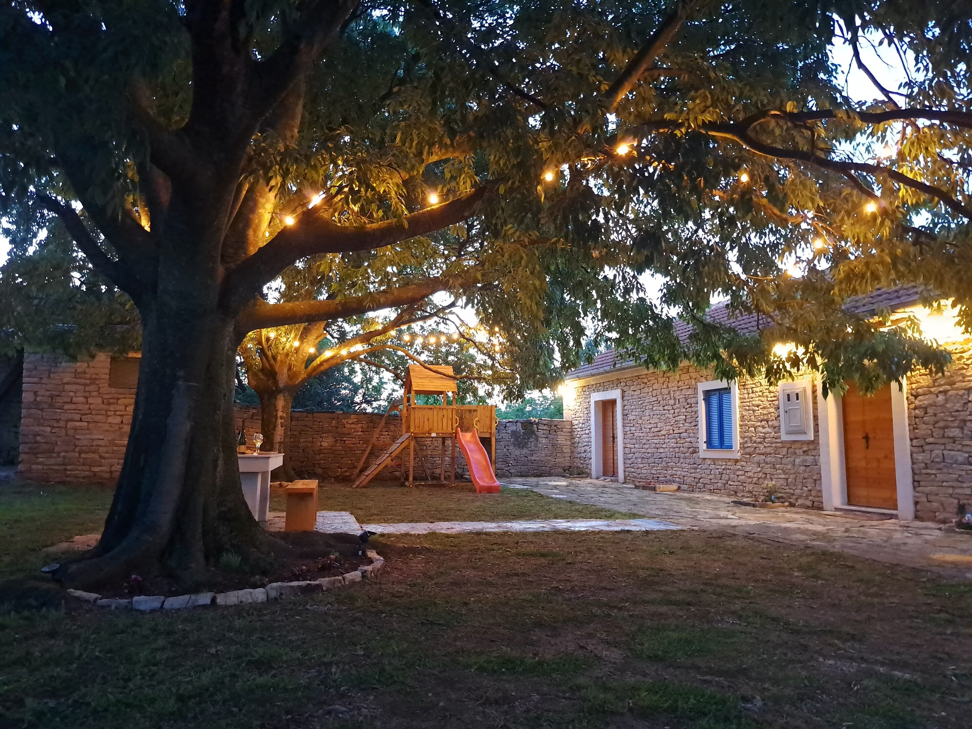Un bâtiment en pierre avec une porte en bois, un mur en briques et un arbre au premier plan.
